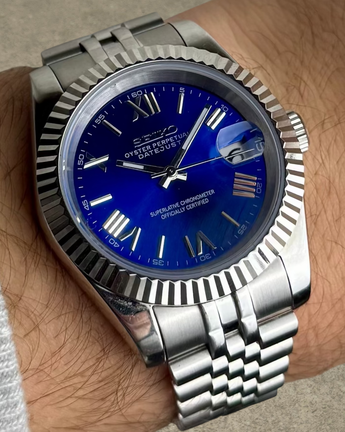 PB TimePiece Classic Date watch with a royal blue dial, Roman numerals, fluted bezel, and stainless steel bracelet.