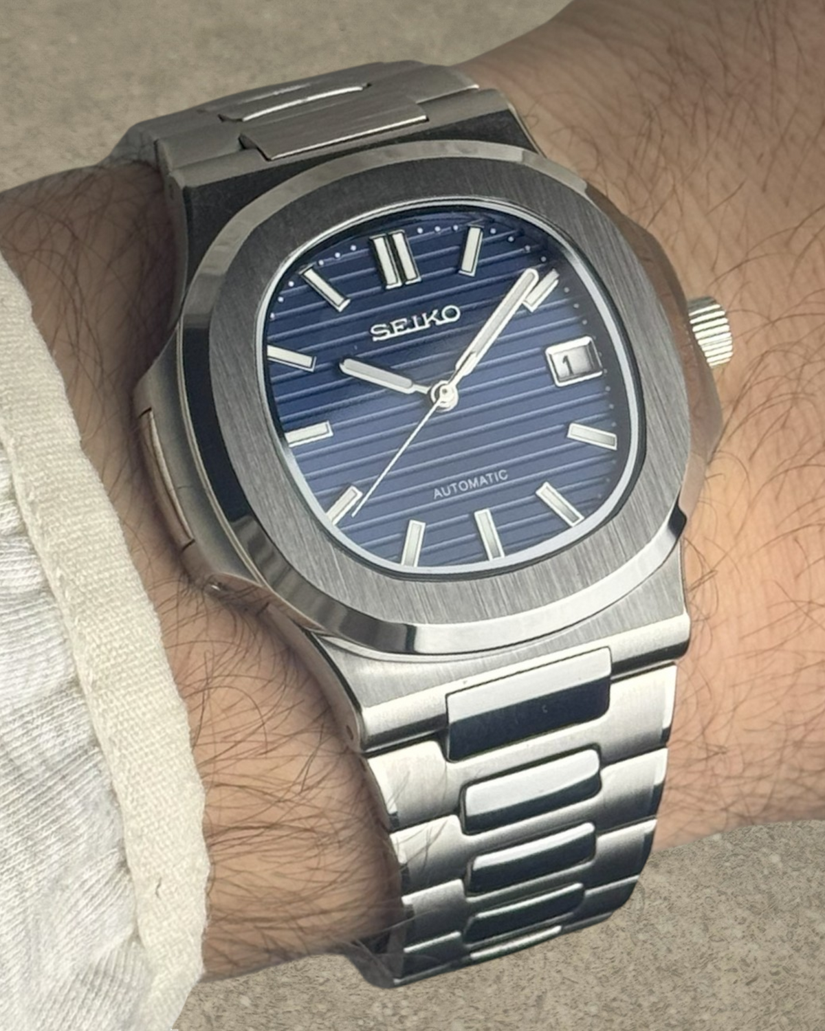PB TimePiece Novara watch with a textured blue dial, stainless steel case, and bracelet on a wrist.