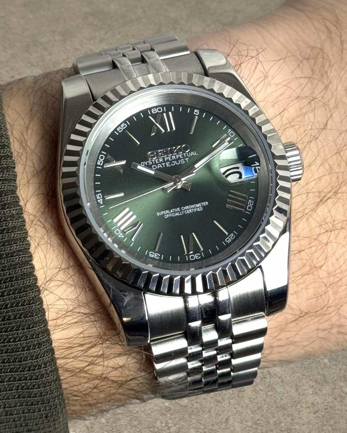 PB TimePiece olive green dial watch with fluted bezel, Roman numerals, and stainless steel jubilee bracelet on wrist