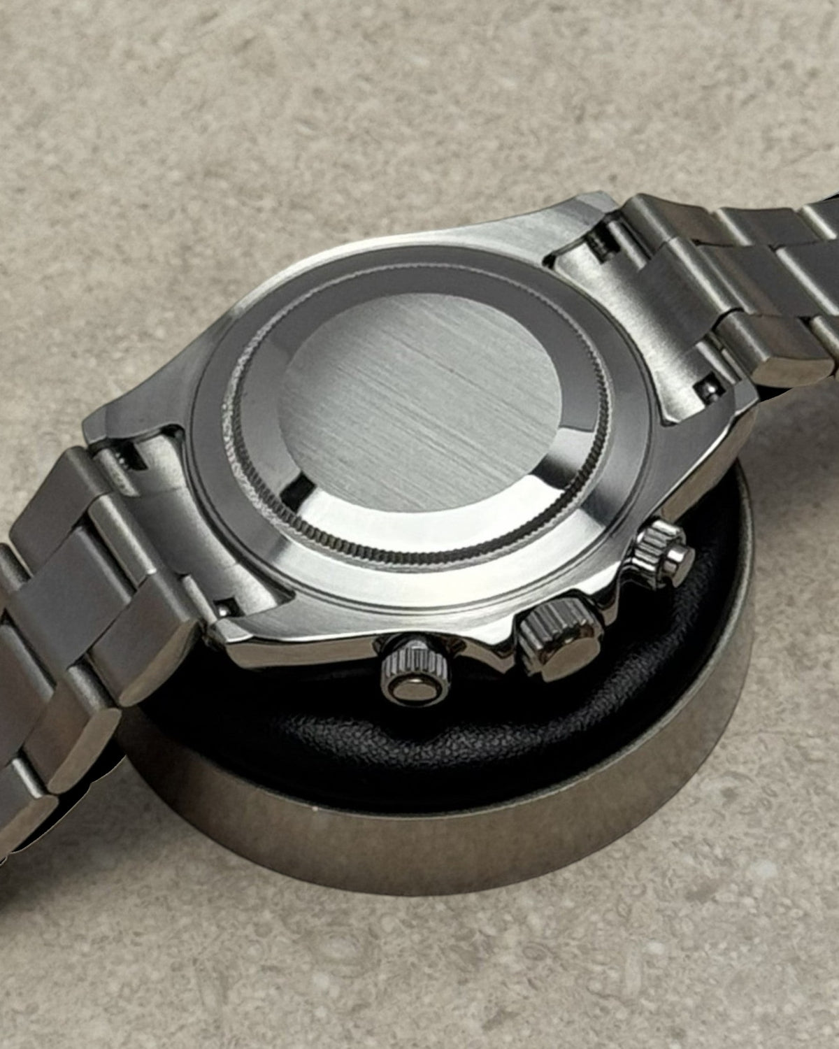 PB TimePiece stainless steel chronograph watch case back with oyster bracelet and pushers on a display stand