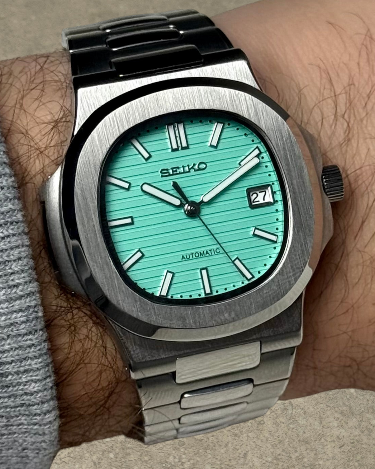 PB TimePiece Novara watch with a textured teal dial, stainless steel case, and bracelet on a wrist.