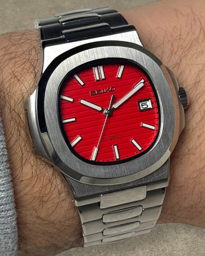 PB TimePiece Novara watch with a textured crimson red dial, stainless steel case, and bracelet on a wrist.