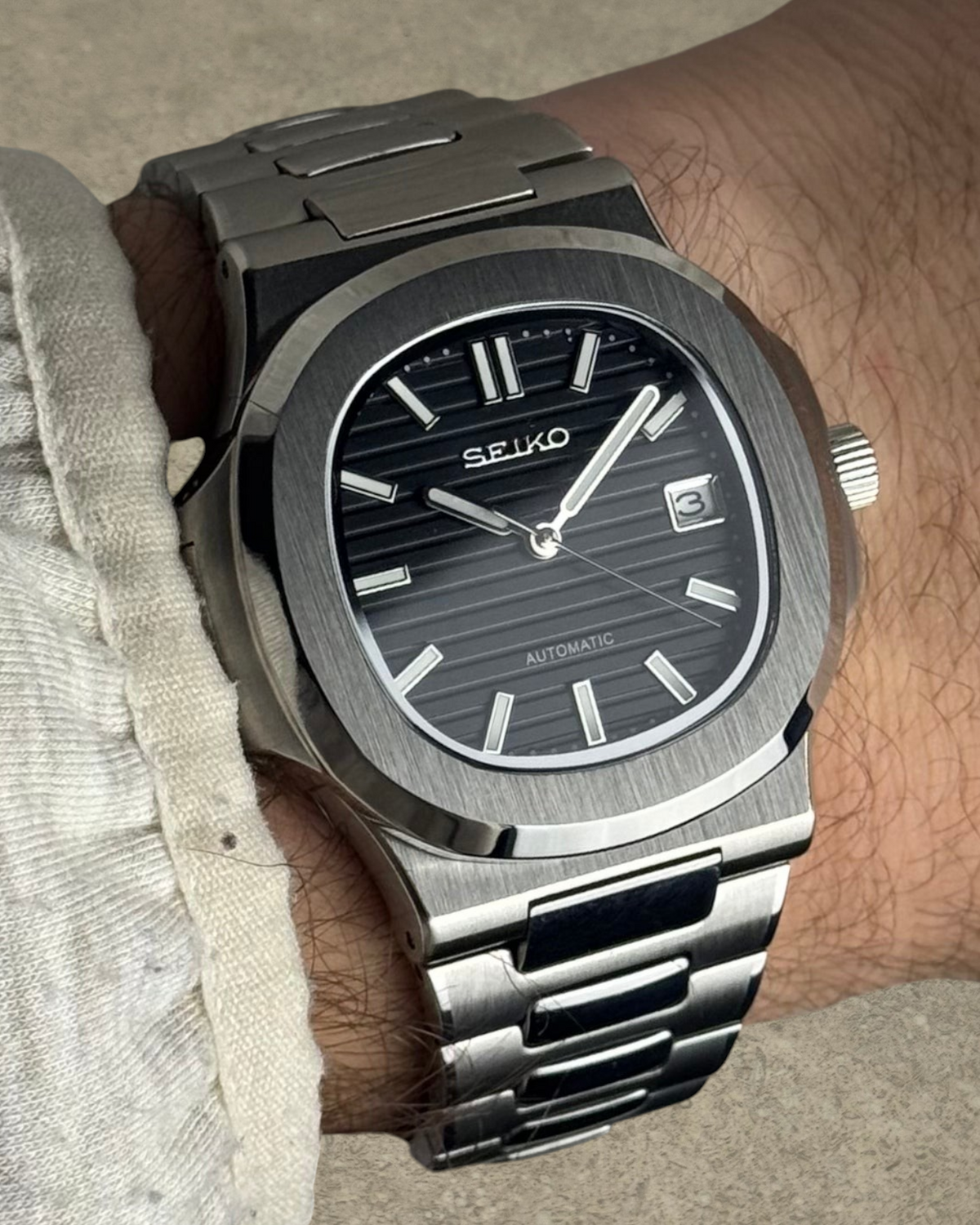PB TimePiece Novara watch with a textured black dial, stainless steel case, and bracelet on a wrist.