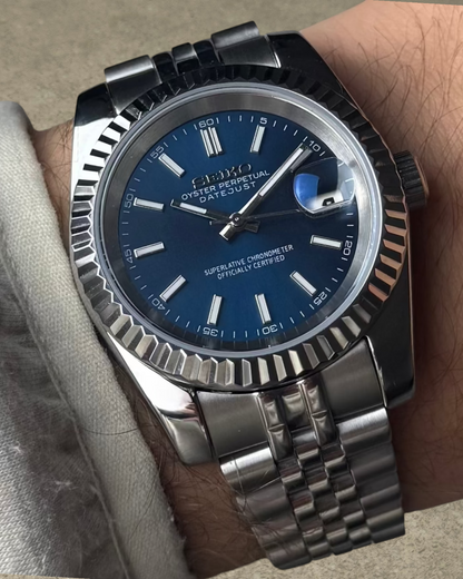 PB TimePiece Classic Date watch with a navy blue dial, stainless steel jubilee bracelet, and fluted bezel on wrist.
