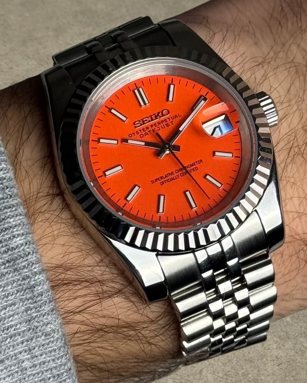 PB TimePiece Classic Date watch with a vibrant orange dial, stainless steel jubilee bracelet, and fluted bezel.