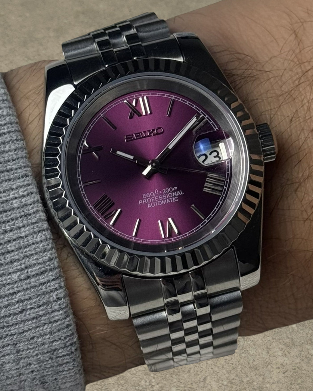 PB TimePiece Classic Date watch with a purple dial, Roman numerals, fluted bezel, and stainless steel jubilee band.