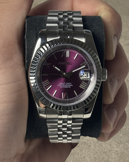 PB TimePiece Classic Date watch with a purple dial, Roman numerals, fluted bezel, and stainless steel jubilee band.