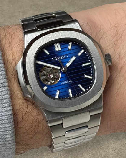 PB TimePiece Novara automatic watch with a blue open heart dial, stainless steel case, and brushed metal bracelet.