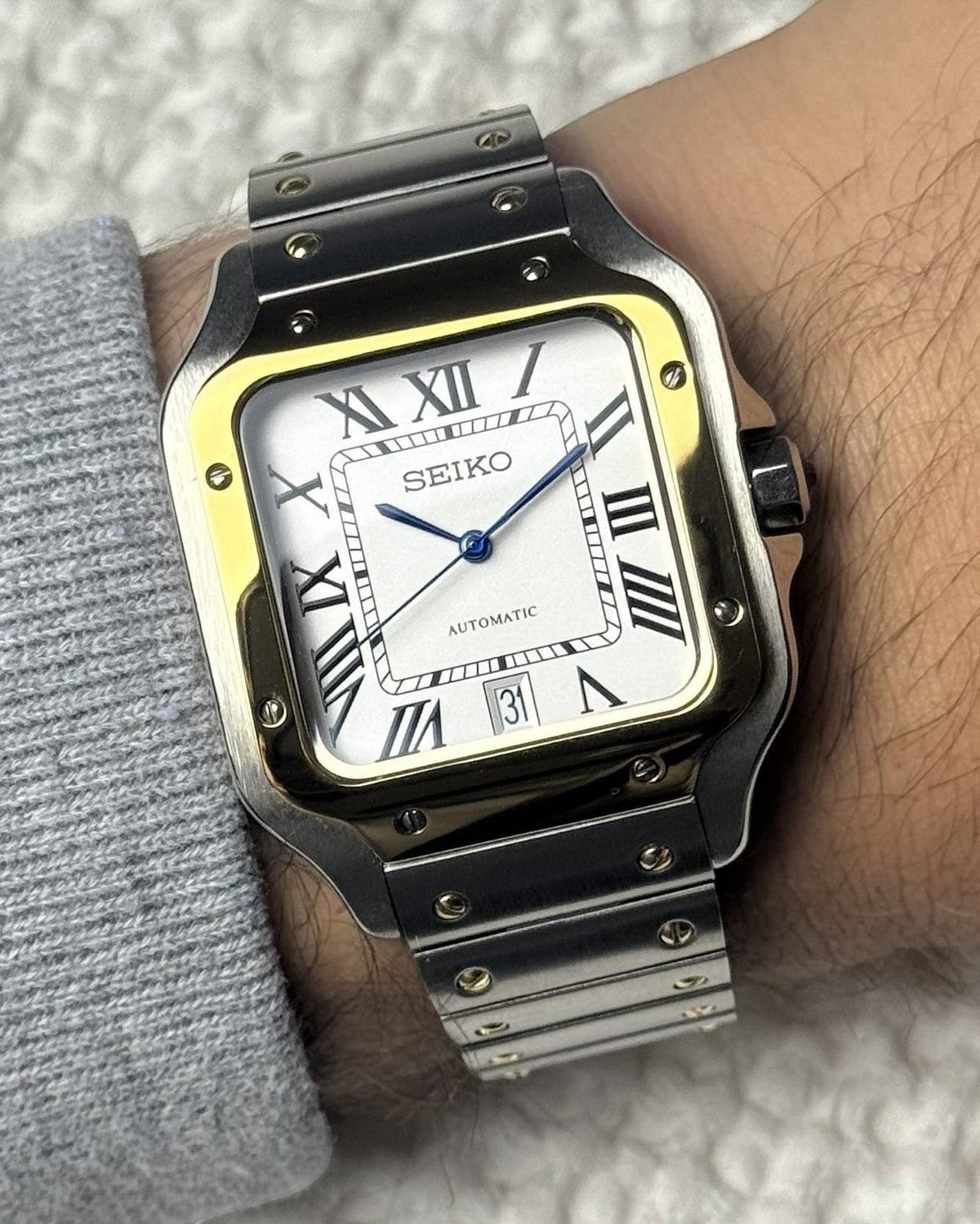 PB TimePiece Aviator watch with two-tone gold and silver stainless steel case, white dial, and blue hands on wrist.