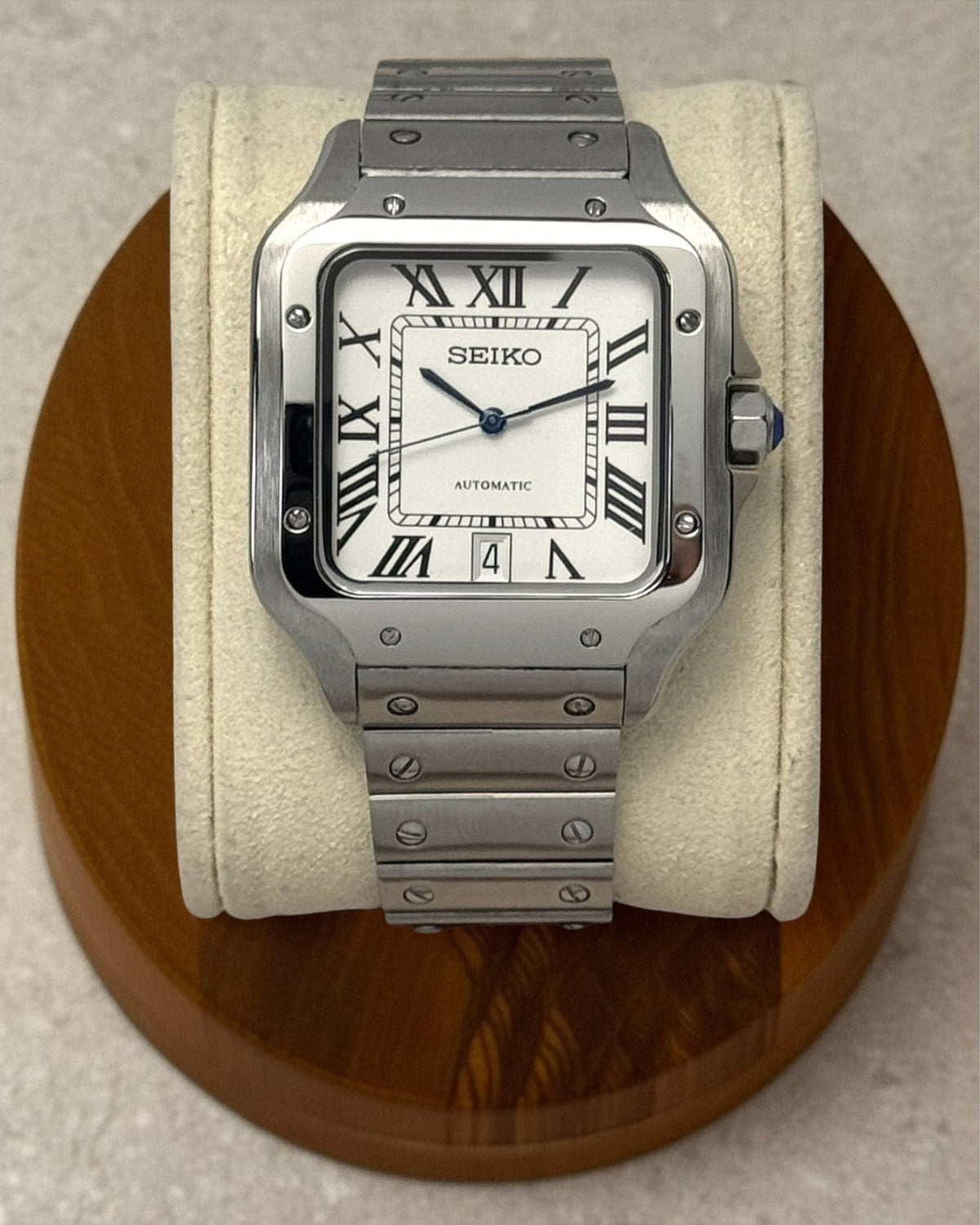 PB TimePiece Aviator watch with white dial, Roman numerals, blue hands, and stainless steel bracelet on display.