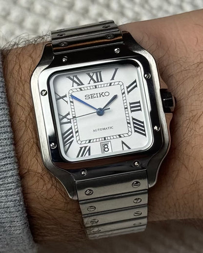 PB TimePiece Aviator watch featuring a white dial, Roman numerals, blue hands, and a stainless steel bracelet.
