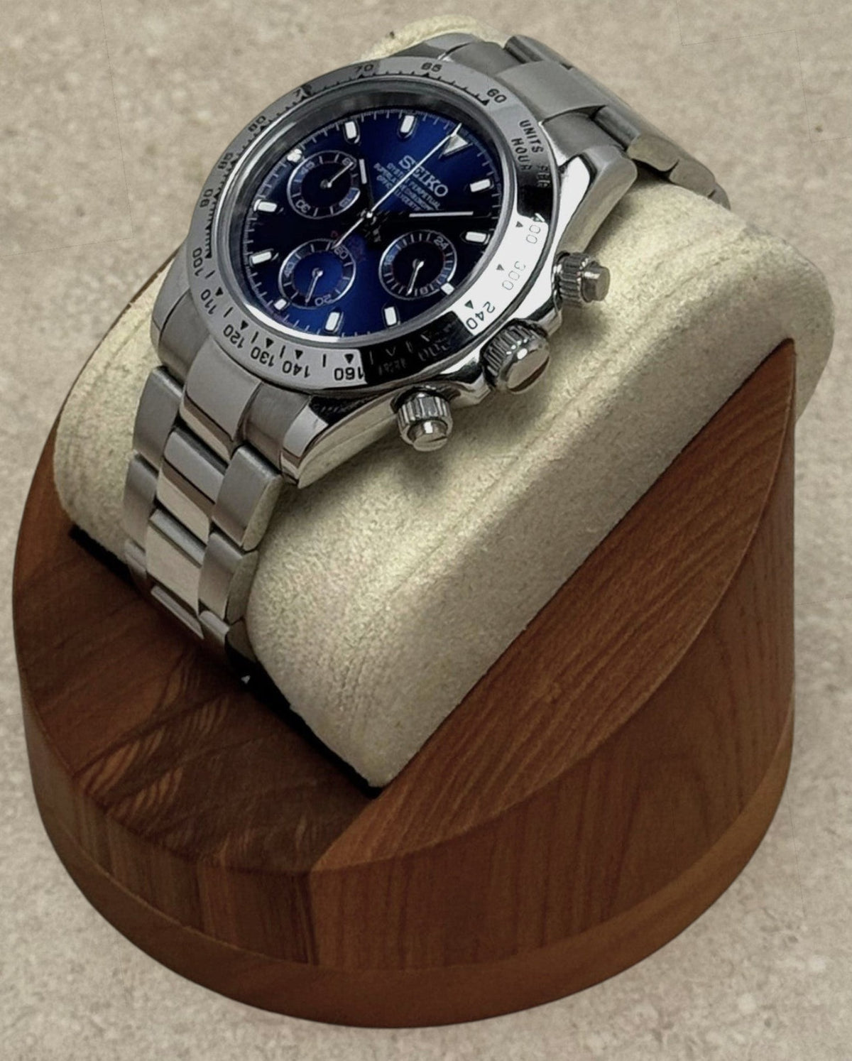 PB TimePiece chronograph watch with a blue dial, stainless steel case, and polished oyster bracelet on a wood stand.