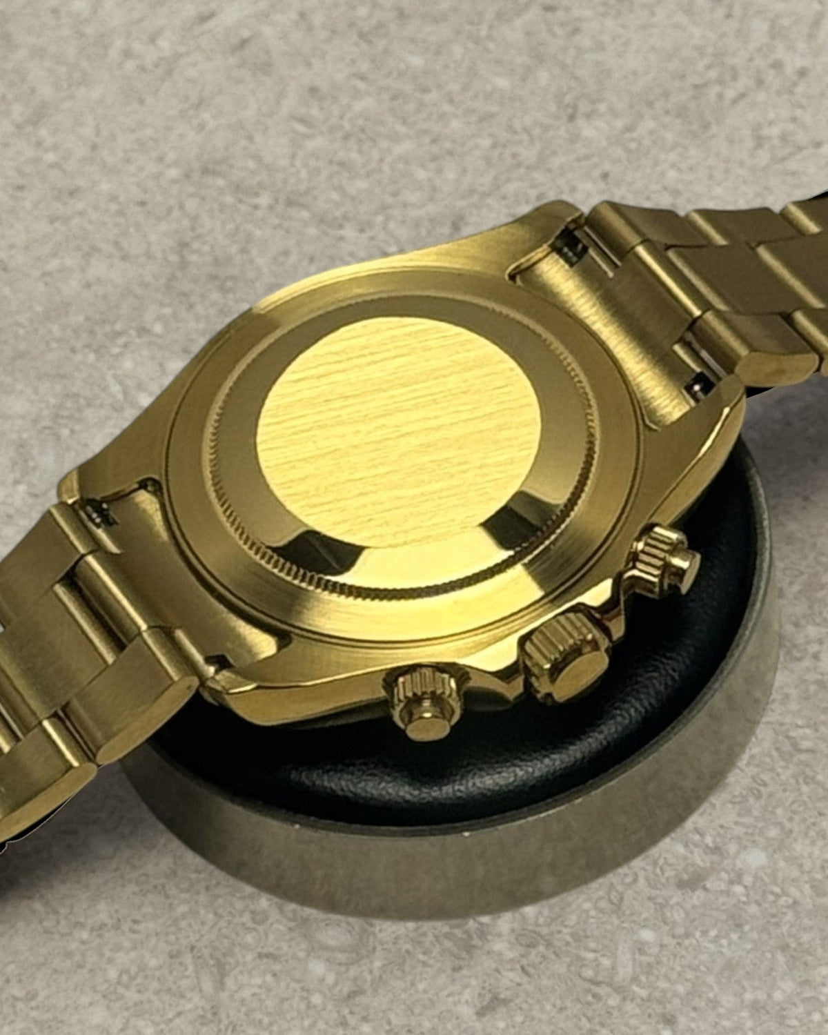 PB TimePiece Bumblebee chronograph watch showing the polished gold case back and oyster bracelet on a display stand.