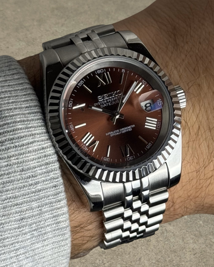 PB TimePiece Classic Date watch with a chocolate dial, Roman numerals, fluted bezel, and stainless steel bracelet.