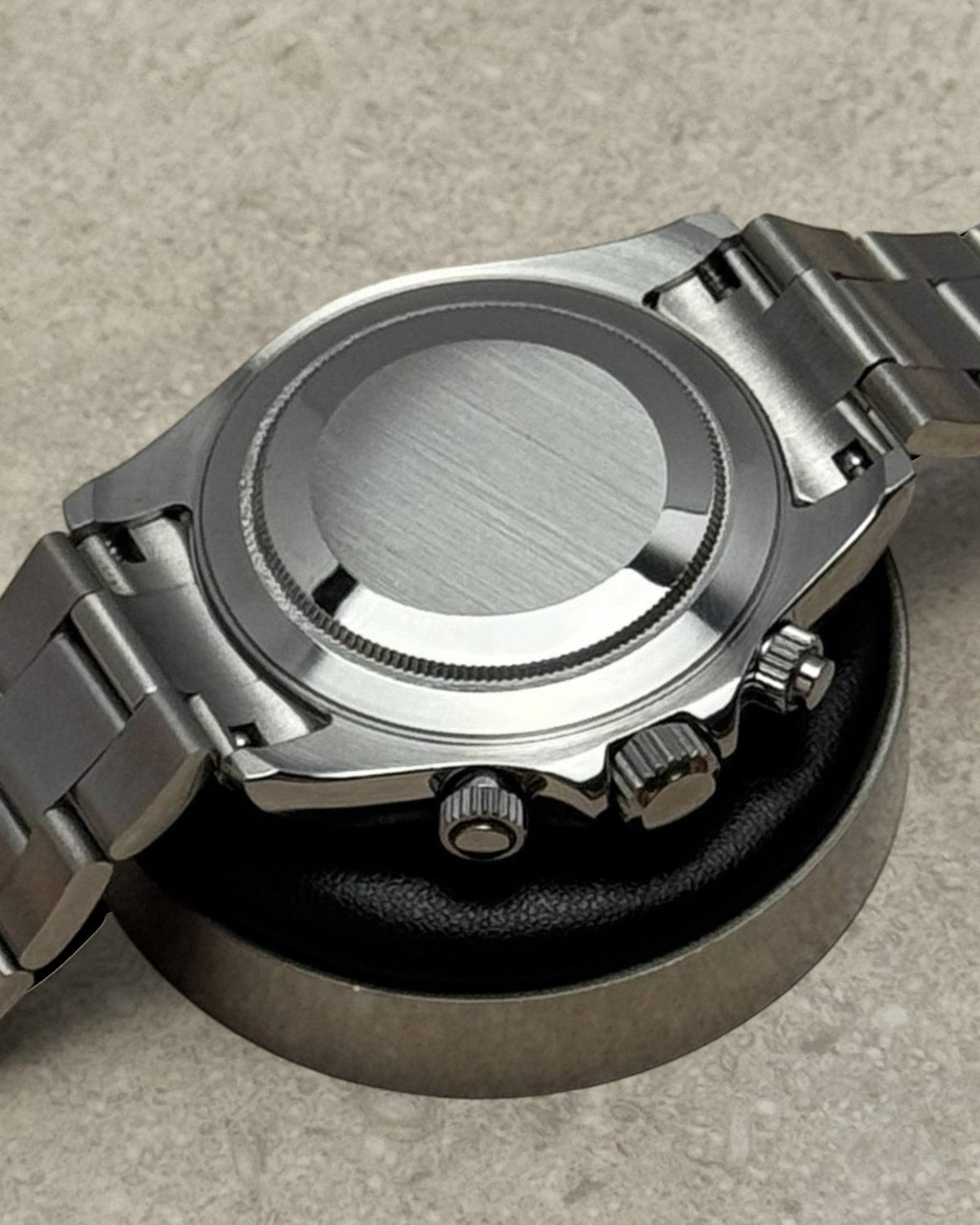 PB TimePiece stainless steel chronograph watch case back showing polished finish and pushers on a display stand