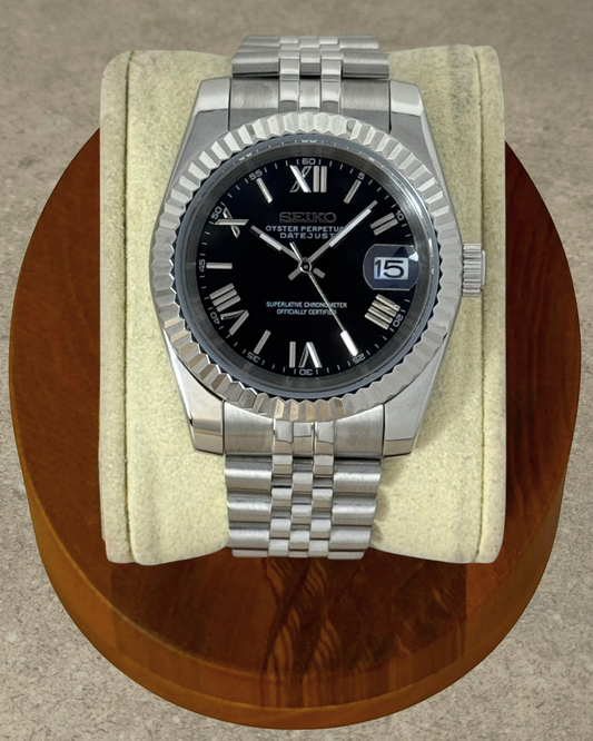 PB TimePiece Classic Date watch with a black dial, Roman numerals, fluted bezel, and stainless steel Jubilee bracelet.