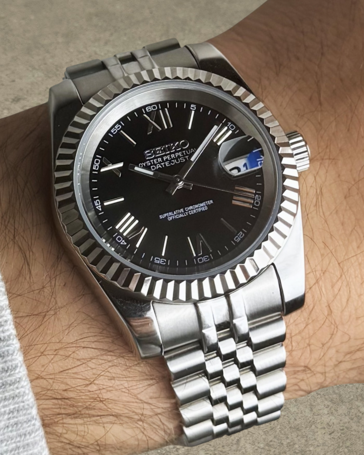 PB TimePiece Classic Date watch with a jet black dial, Roman numerals, fluted bezel, and stainless steel bracelet.