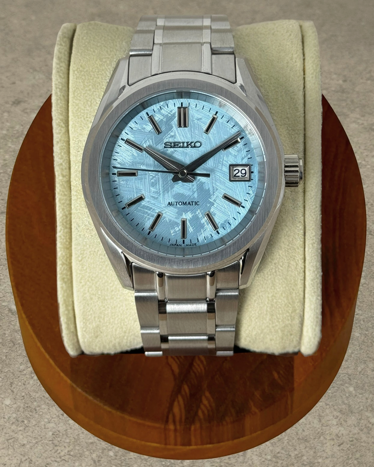 PB TimePiece Heritage watch with ice blue textured dial, stainless steel case, and bracelet on a display cushion.