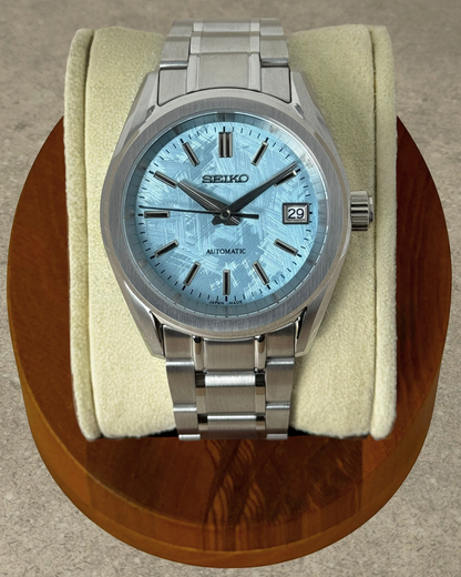 PB TimePiece Heritage watch with ice blue textured dial, stainless steel case, and bracelet on a display cushion.