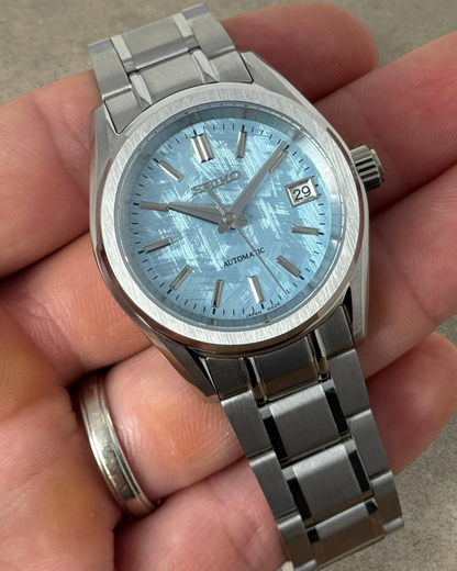 PB TimePiece Heritage watch with an ice blue textured dial, stainless steel case, and bracelet held in a hand.