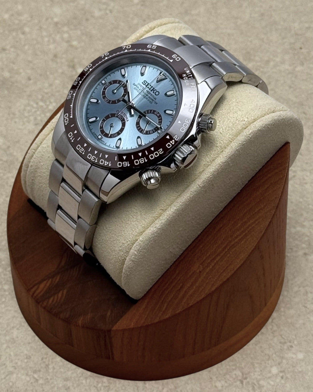 PB TimePiece chronograph watch with ice blue dial, brown bezel, and stainless steel oyster bracelet on display stand.