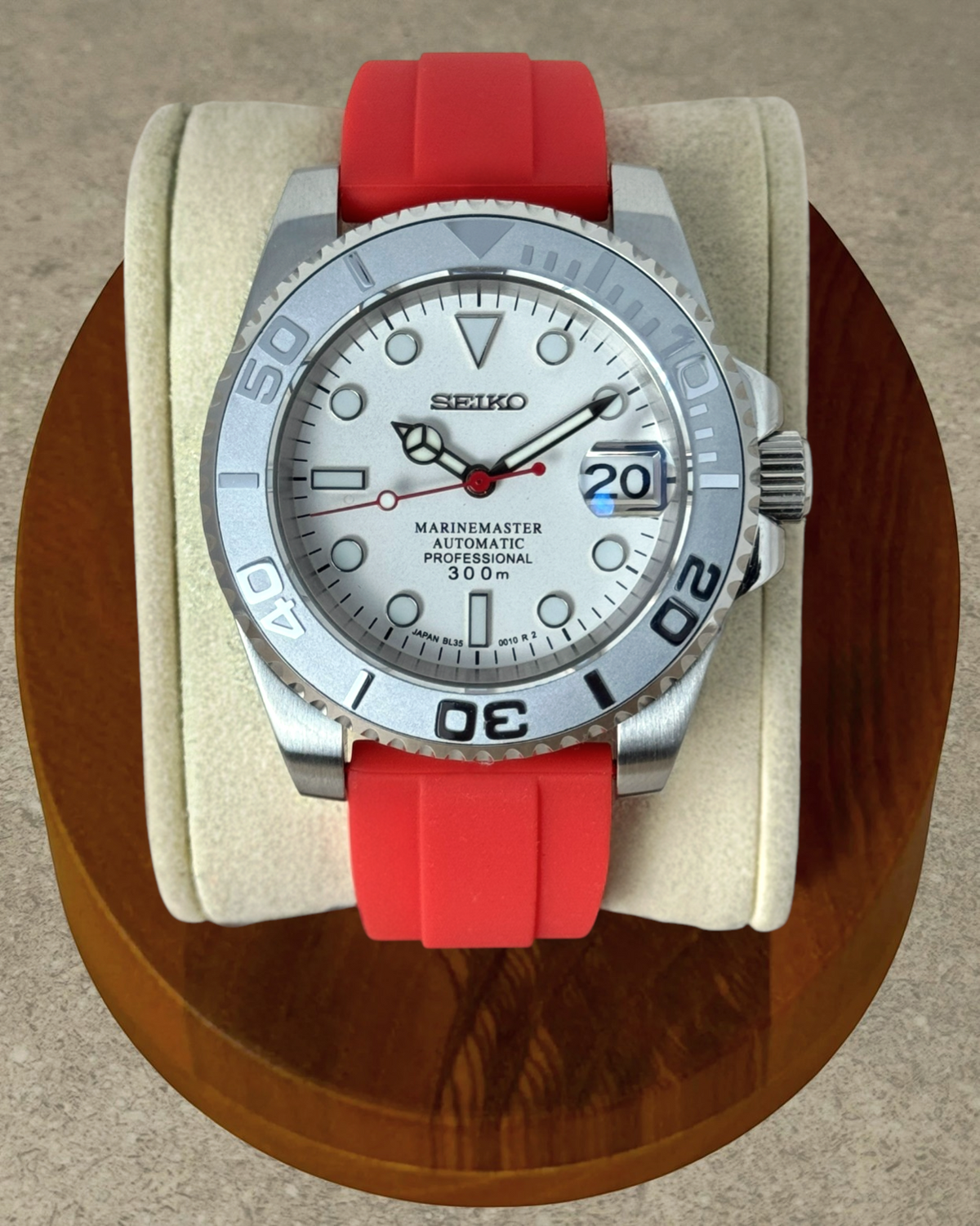 PB TimePiece Marinemaster watch with white dial, matte gray bezel, and vibrant red rubber strap on a display stand.