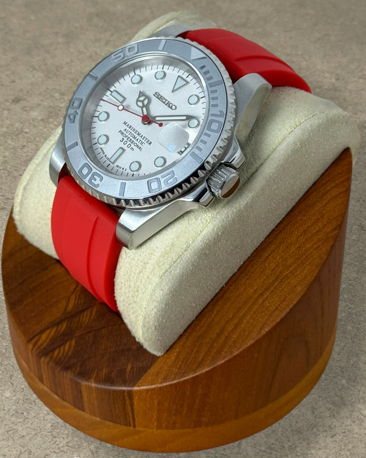 PB TimePiece Marinemaster watch with a white dial, red rubber strap, and matte gray rotating bezel on a display stand