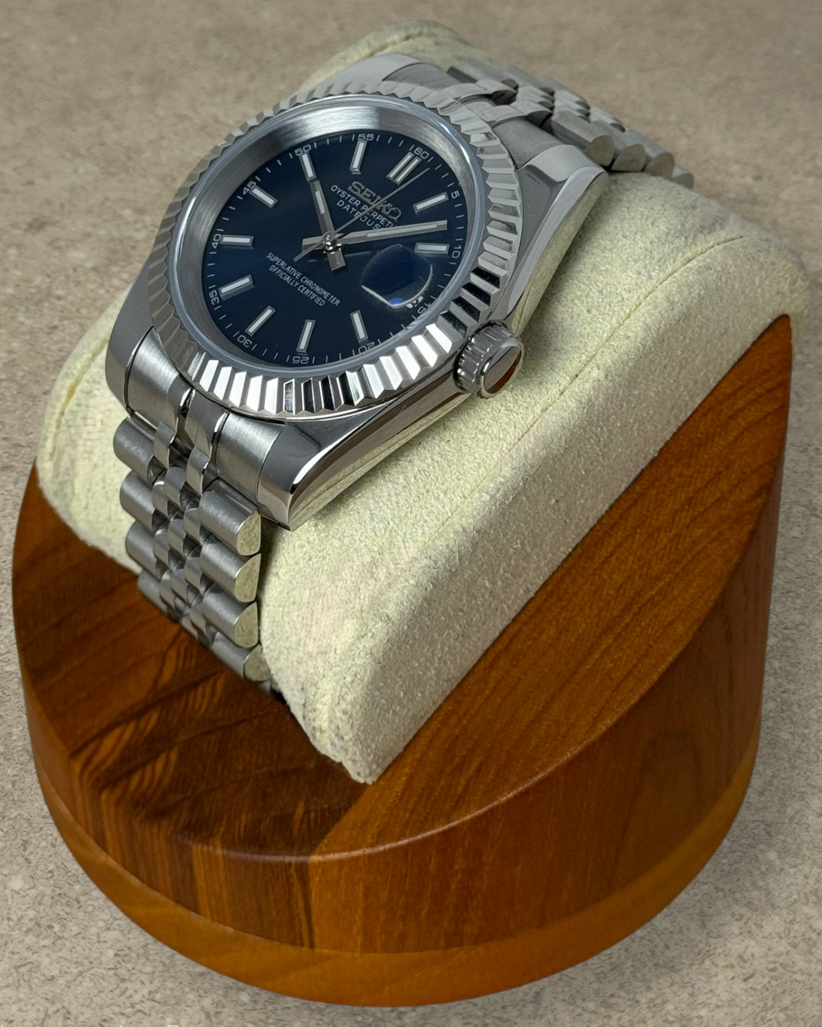 PB TimePiece Classic Date watch with a navy blue dial, stainless steel jubilee bracelet, and fluted bezel on a stand.