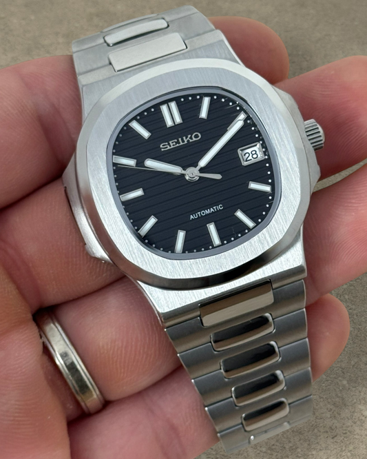 PB TimePiece Novara automatic watch with a textured black dial, stainless steel case, and brushed metal bracelet.