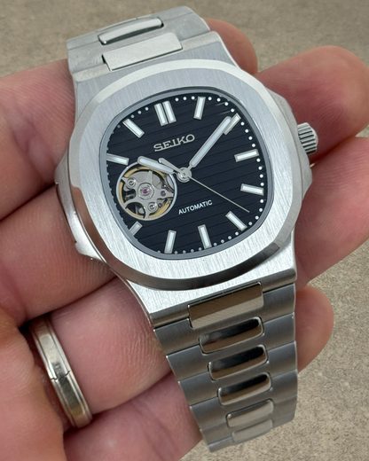 PB TimePiece Novara automatic watch with a black open heart dial, stainless steel case, and brushed link bracelet.
