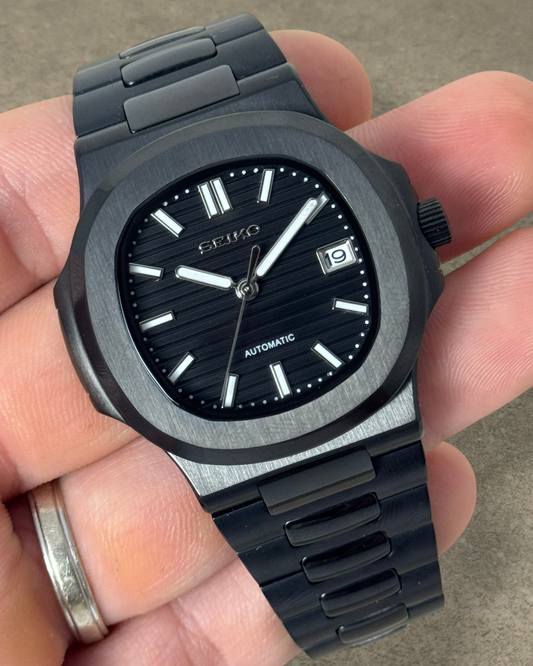 PB TimePiece Novara watch with a black stainless steel case, textured black dial, and matching black bracelet.
