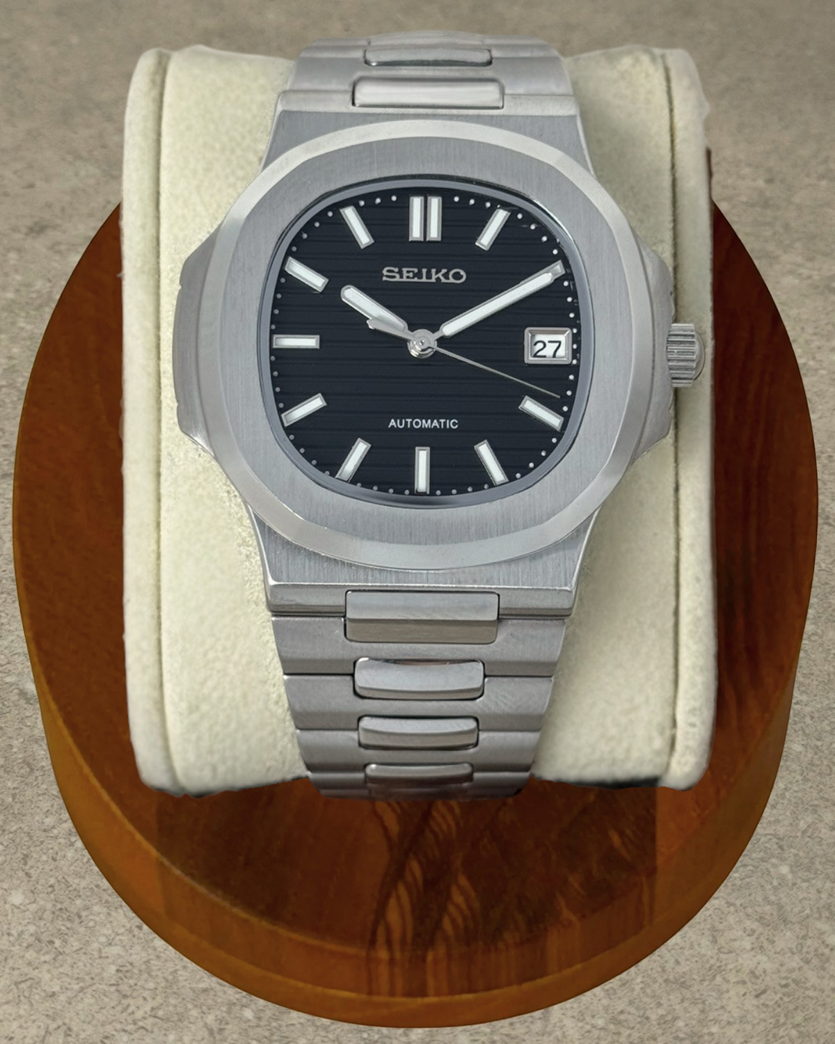 PB TimePiece Novara watch with a textured black dial, stainless steel case, and brushed bracelet on a display stand.