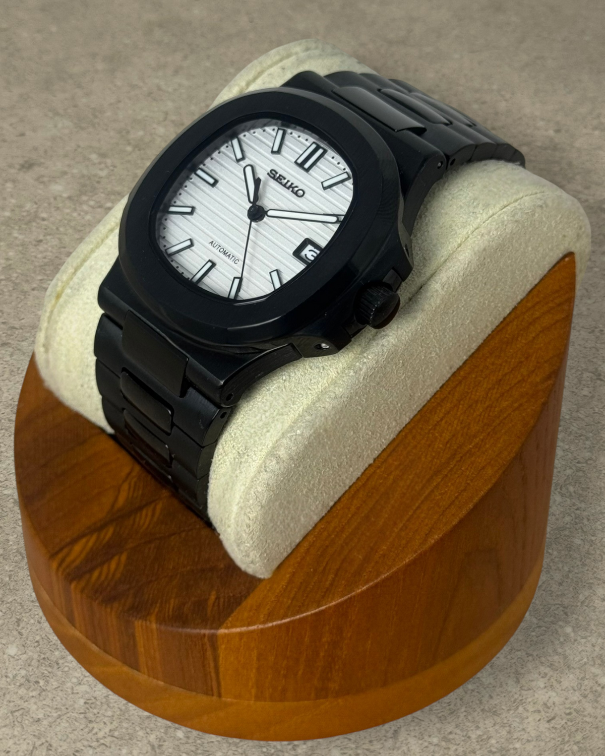 PB TimePiece Novara watch with a black stainless steel case, bracelet, and a textured white dial on a wooden stand.