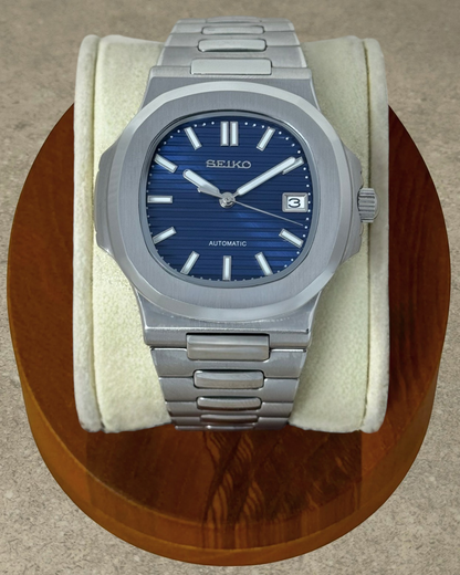 PB TimePiece Novara automatic watch with a textured blue dial, stainless steel case, and brushed link bracelet.