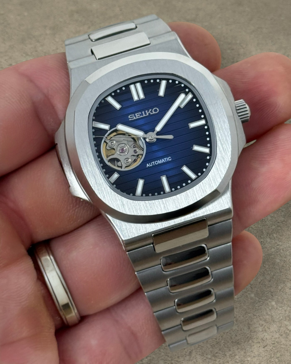 PB TimePiece Novara automatic watch with a blue open heart dial, stainless steel case, and brushed bracelet.