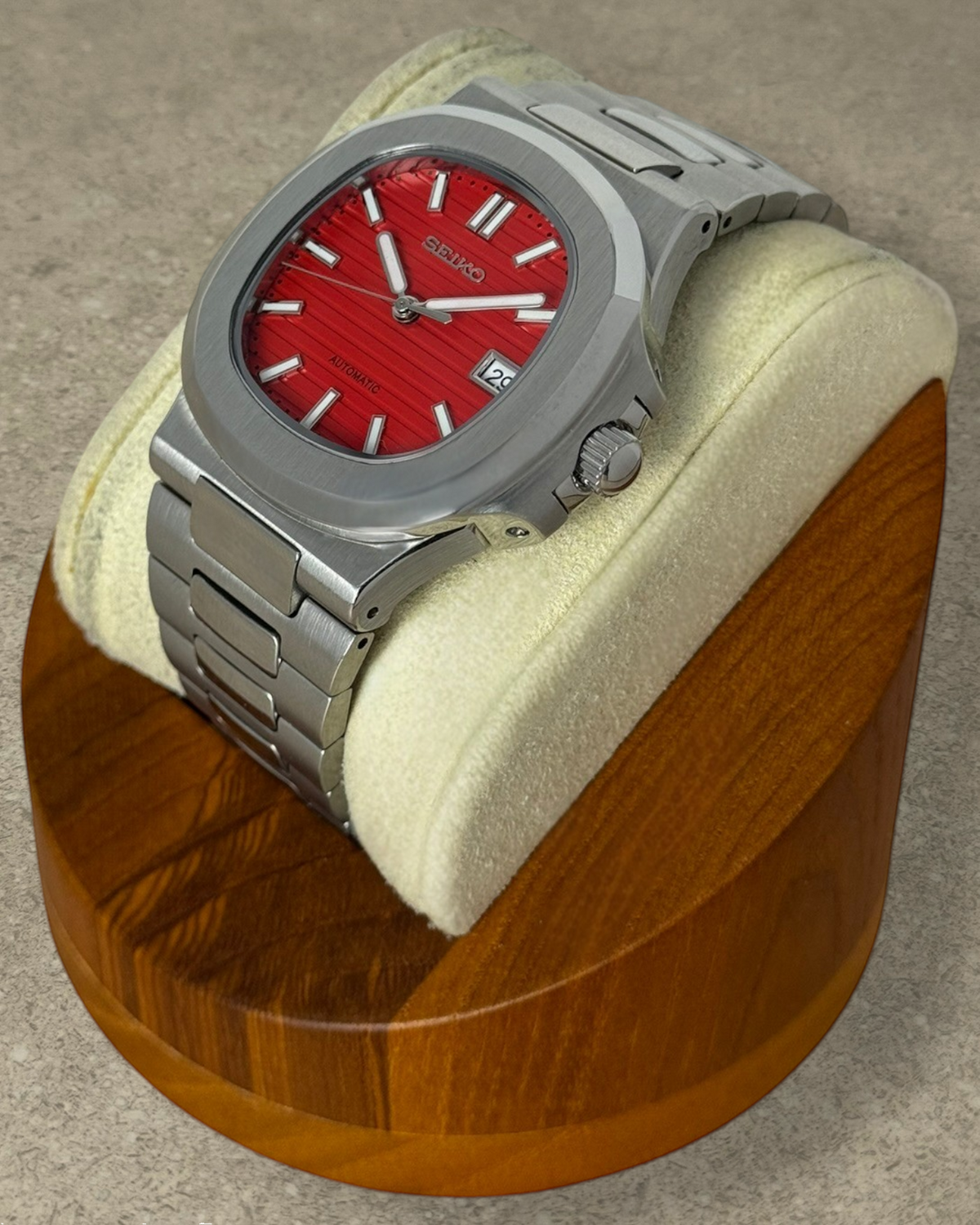 PB TimePiece Novara watch with a textured crimson red dial, stainless steel case, and bracelet on a wooden stand.