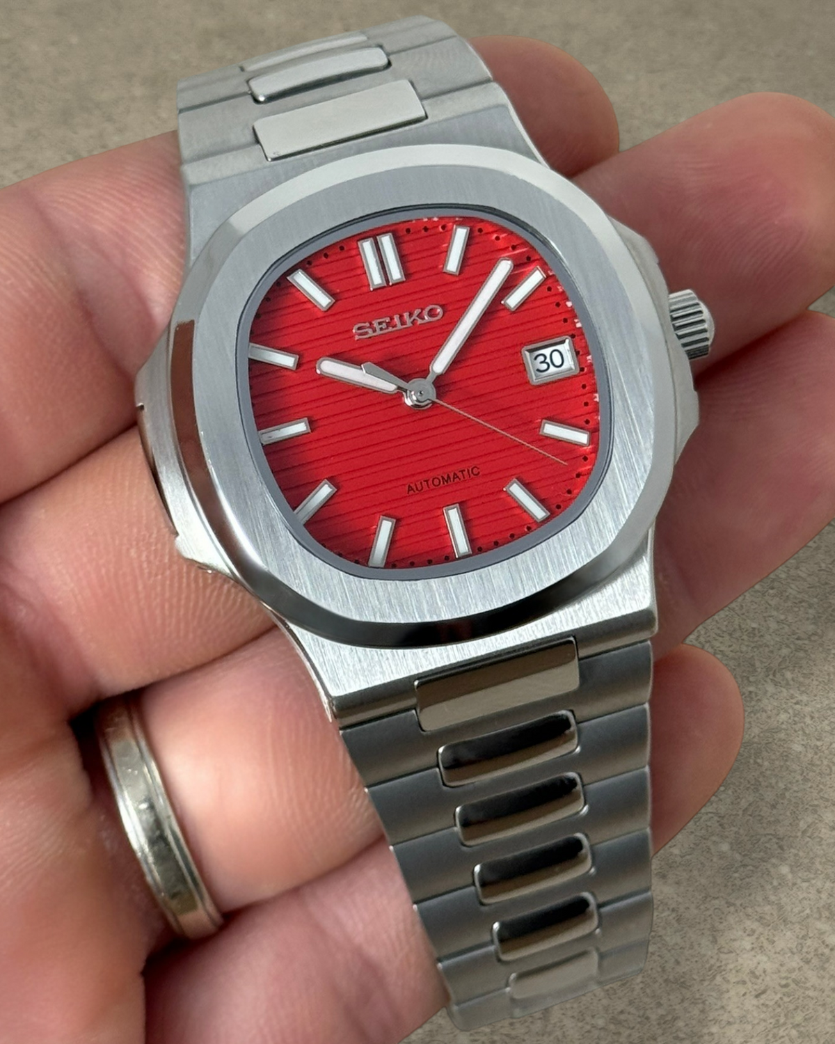 PB TimePiece Novara watch with a textured crimson red dial, stainless steel case, and brushed metal bracelet.