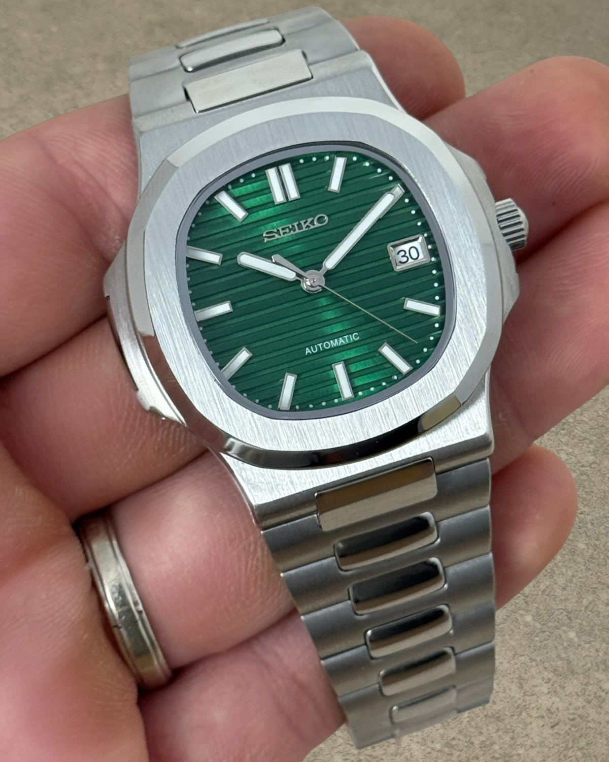 PB TimePiece Novara watch with a textured emerald green dial, stainless steel case, and brushed link bracelet.