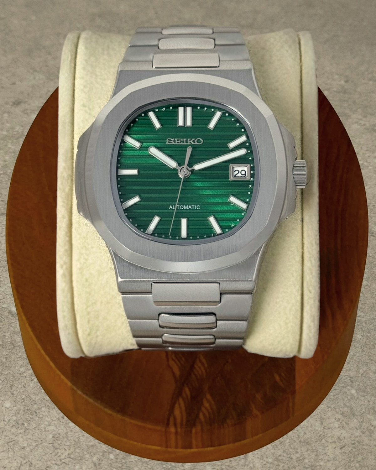 PB TimePiece Novara watch with a textured emerald green dial, stainless steel case, and bracelet on a wooden stand.