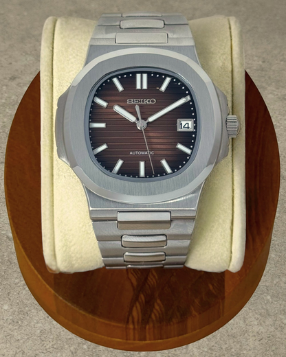 PB TimePiece Novara watch with a textured ombre brown dial, stainless steel case, and bracelet on a wooden stand.