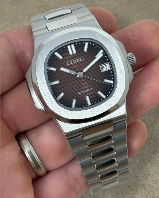 PB TimePiece Novara watch with a textured ombre brown dial, stainless steel case, and bracelet held in a hand.