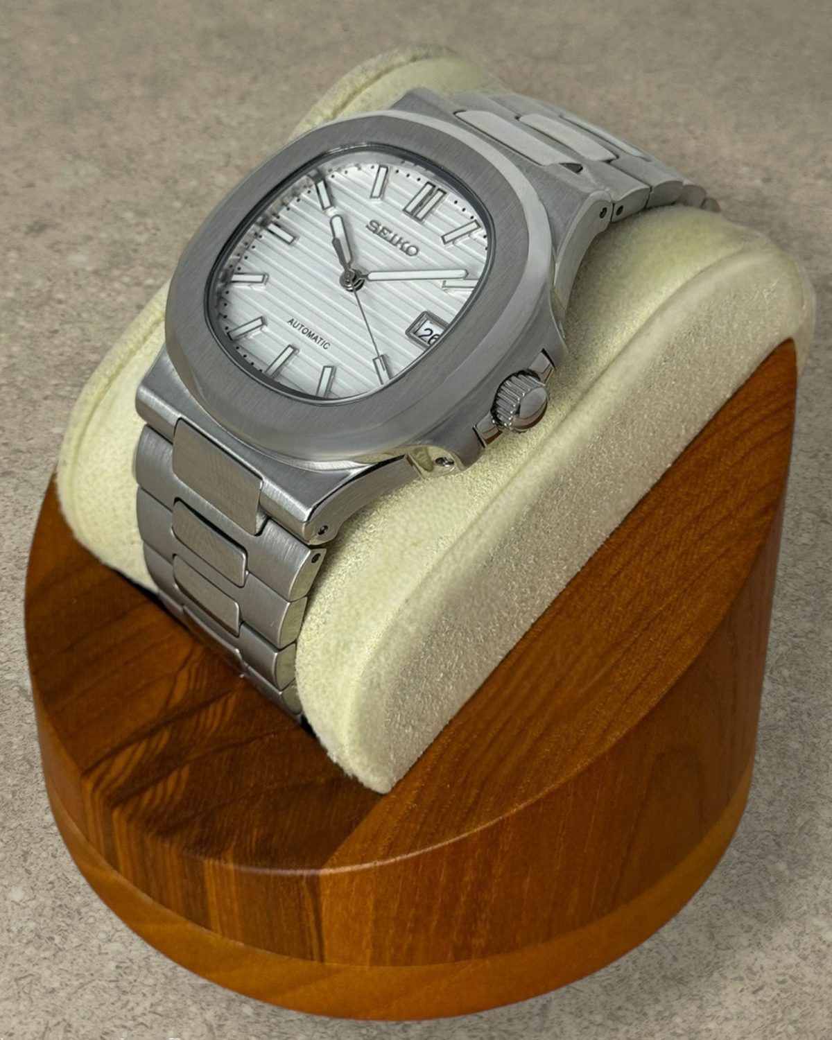 PB TimePiece Novara watch with a textured white dial, stainless steel case, and bracelet on a wooden display stand.