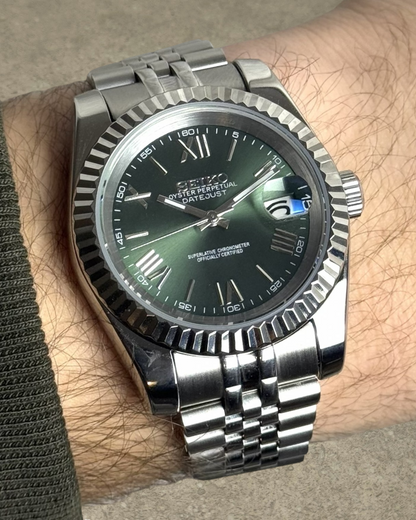 PB TimePiece olive green dial watch with fluted bezel, Roman numerals, and stainless steel jubilee bracelet on wrist