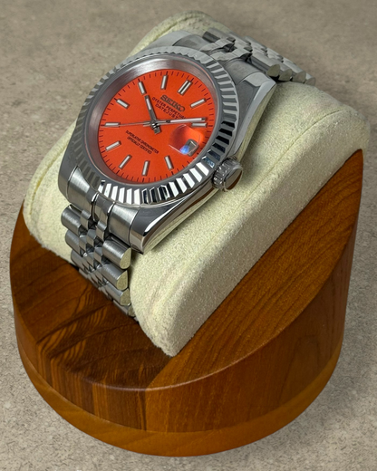 PB TimePiece Classic Date watch with a vibrant orange dial, fluted bezel, and stainless steel jubilee bracelet.