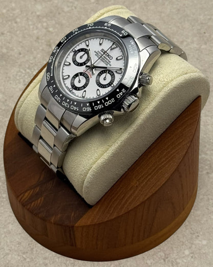 PB TimePiece Panda chronograph watch with white dial, black bezel, and stainless steel oyster bracelet on a stand.