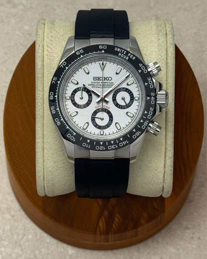 PB TimePiece Panda chronograph watch with white dial, black bezel, and black rubber strap on a wooden display stand.