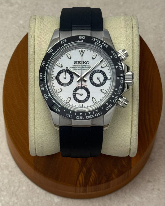 PB TimePiece Panda chronograph watch with white dial, black bezel, and black rubber strap on a wooden display stand.