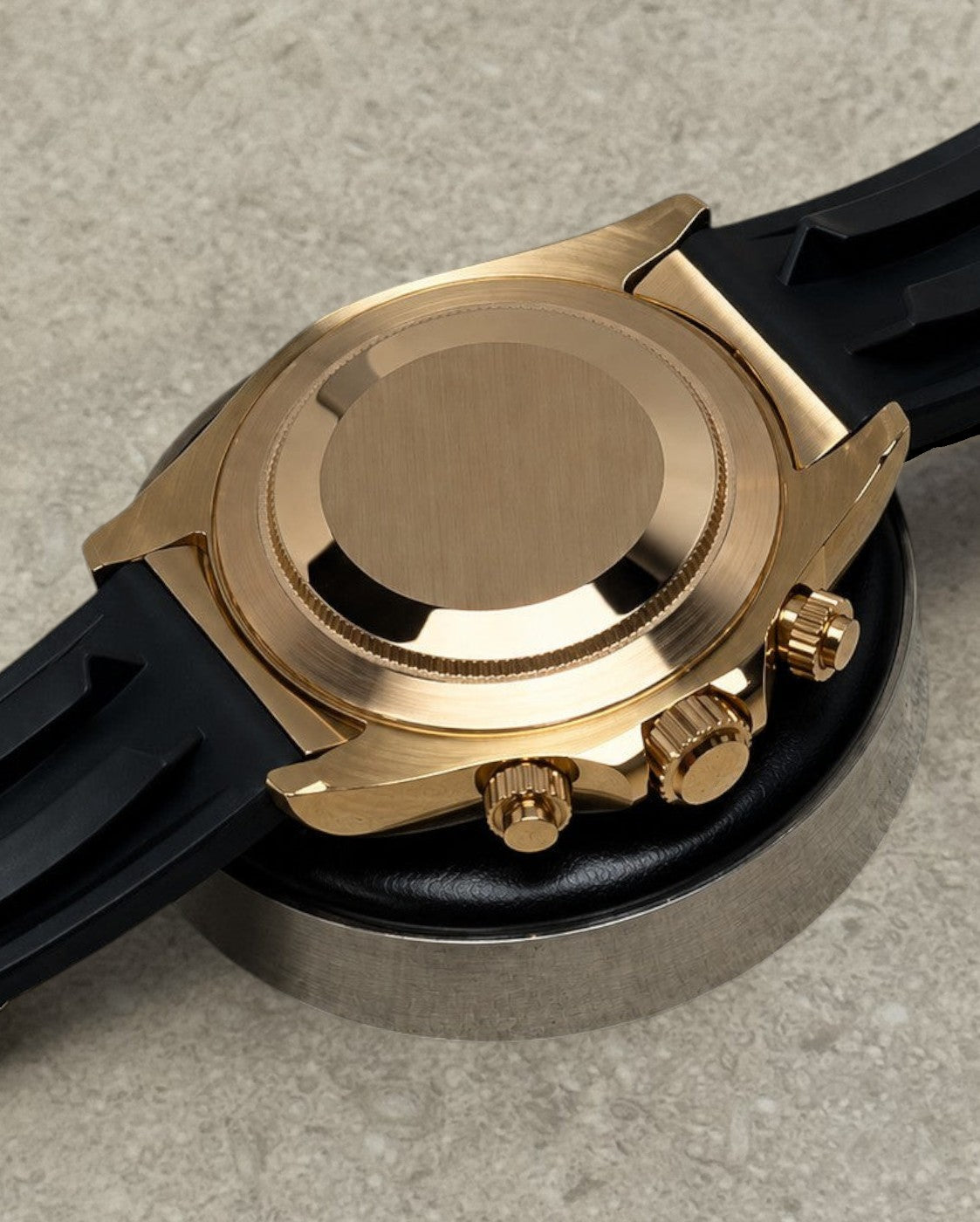 PB TimePiece rose gold chronograph watch case back view with black rubber strap on a textured surface