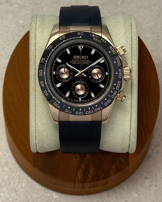 PB TimePiece rose gold chronograph watch with a black dial, black rubber strap, and 39mm case on a display stand.