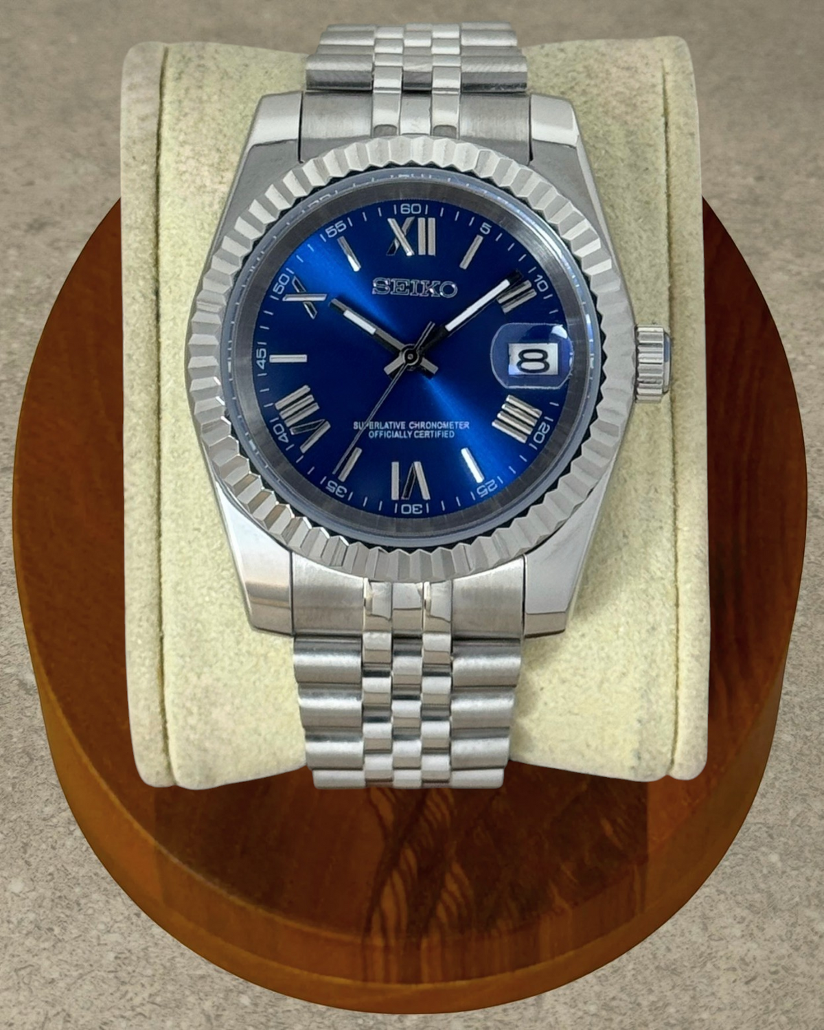 PB TimePiece Classic Date watch with a royal blue dial, Roman numerals, fluted bezel, and stainless steel bracelet.